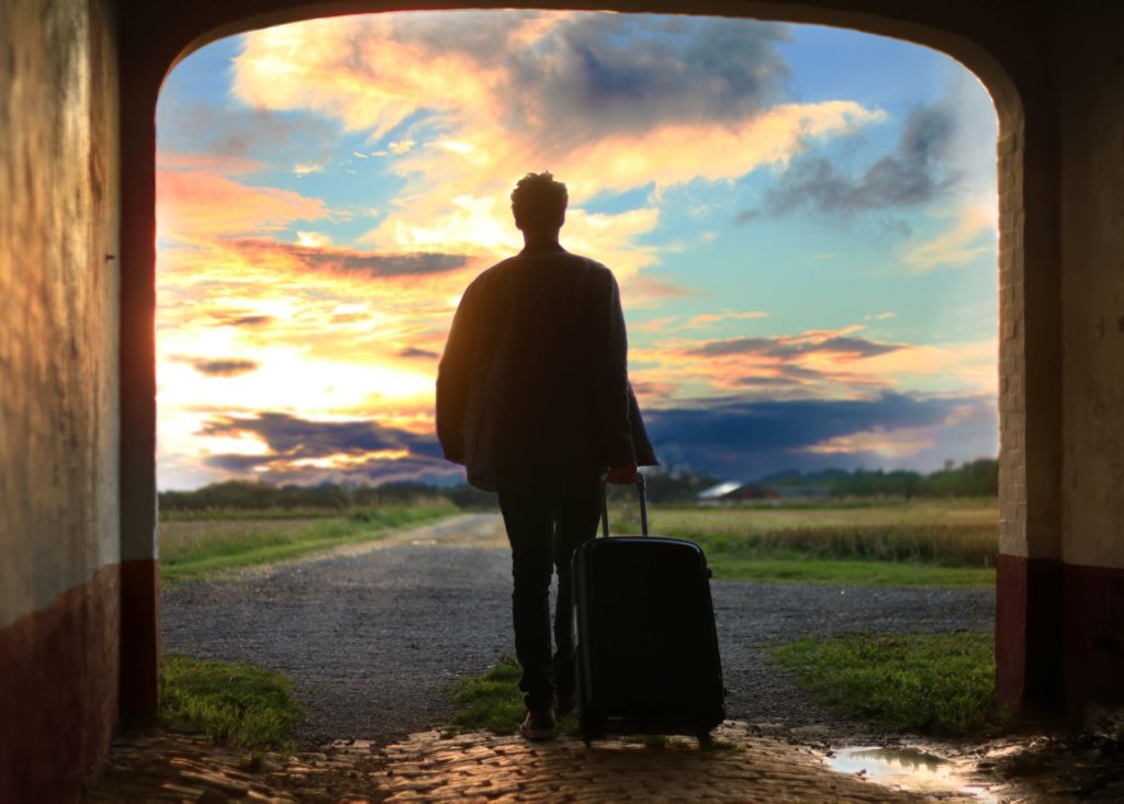 man with luggage walking into a sunset